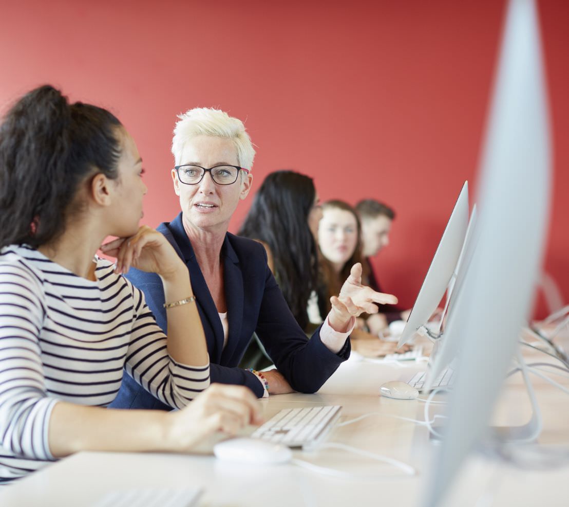 Photo of five people working at a long table with the focus on two women working together