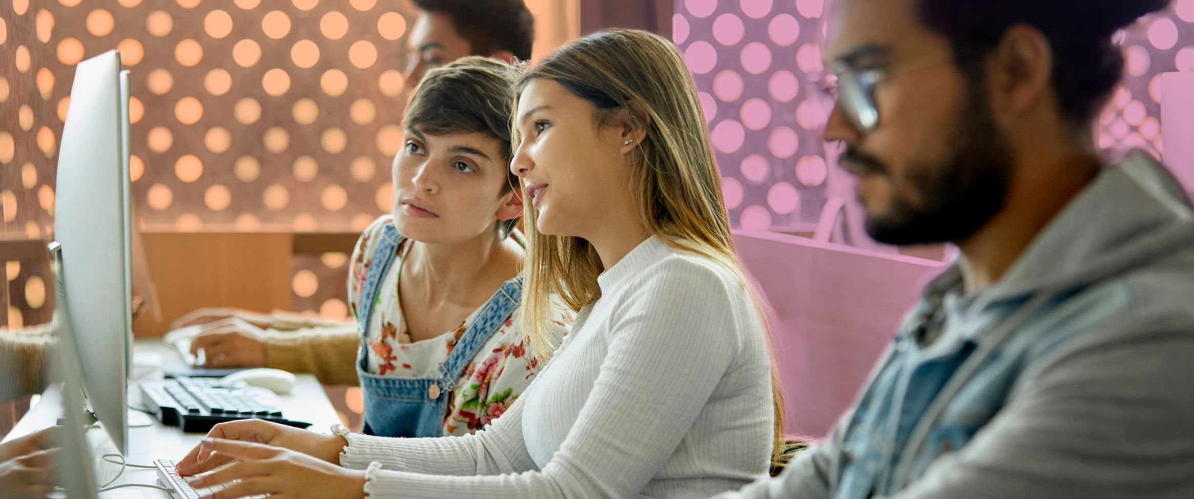 Photo of four students working with the focus on two women collaborating at a computer